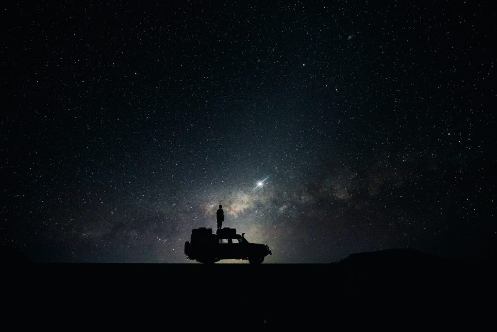Man on top of jeep looking into space with a telescope.